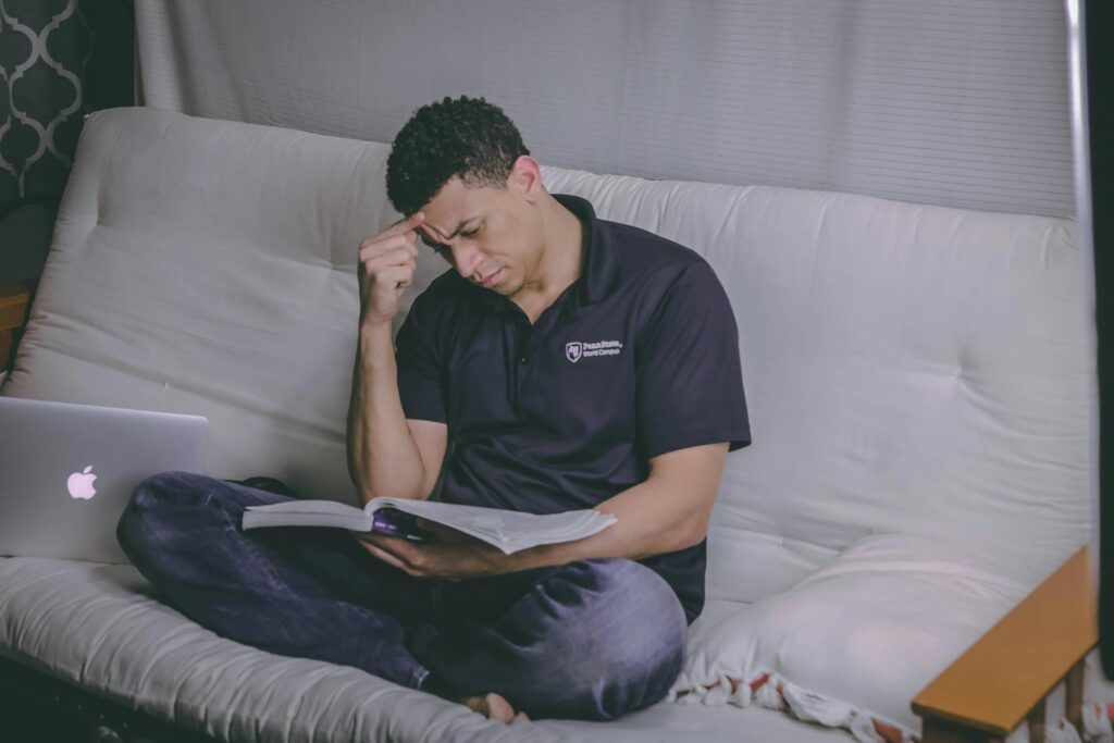 A male student Sitting on Sofa Reading Book