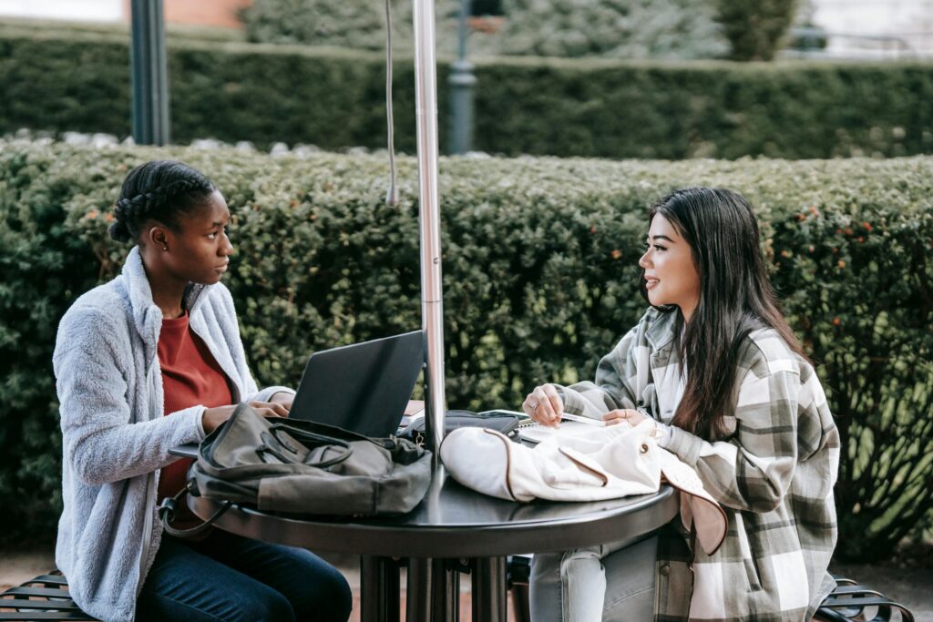 Diverse female students with laptop in campus sitting and talking