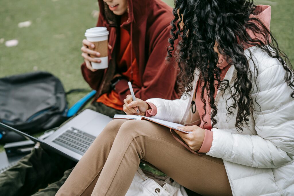 Two female students studying together on grassy lawn
