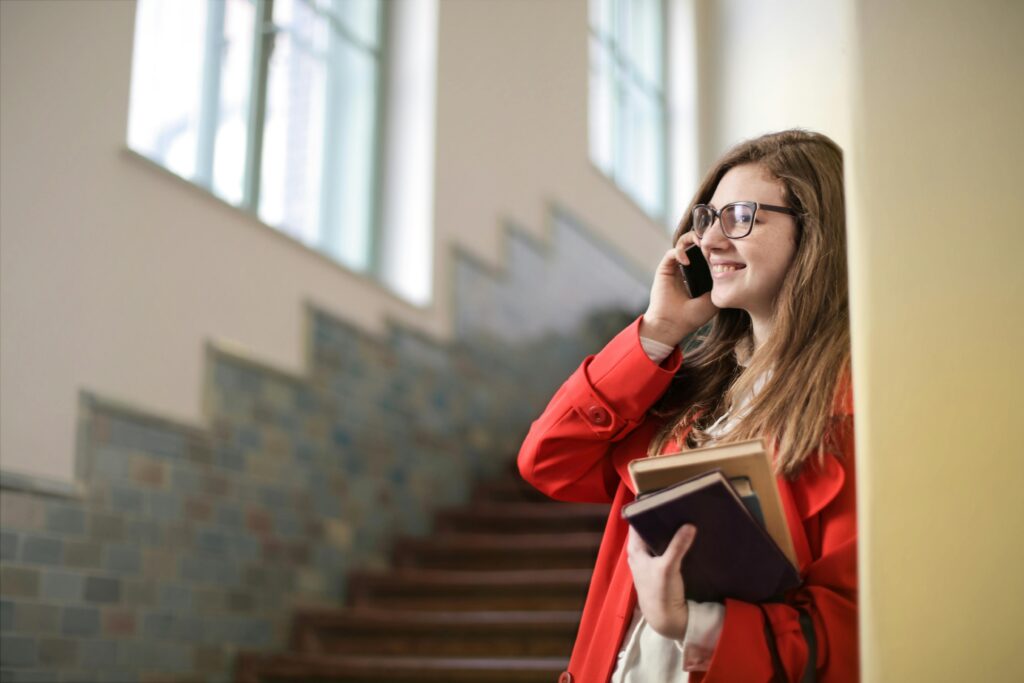 Student in Red Coat and Black Framed Eyeglasses While Holding Books