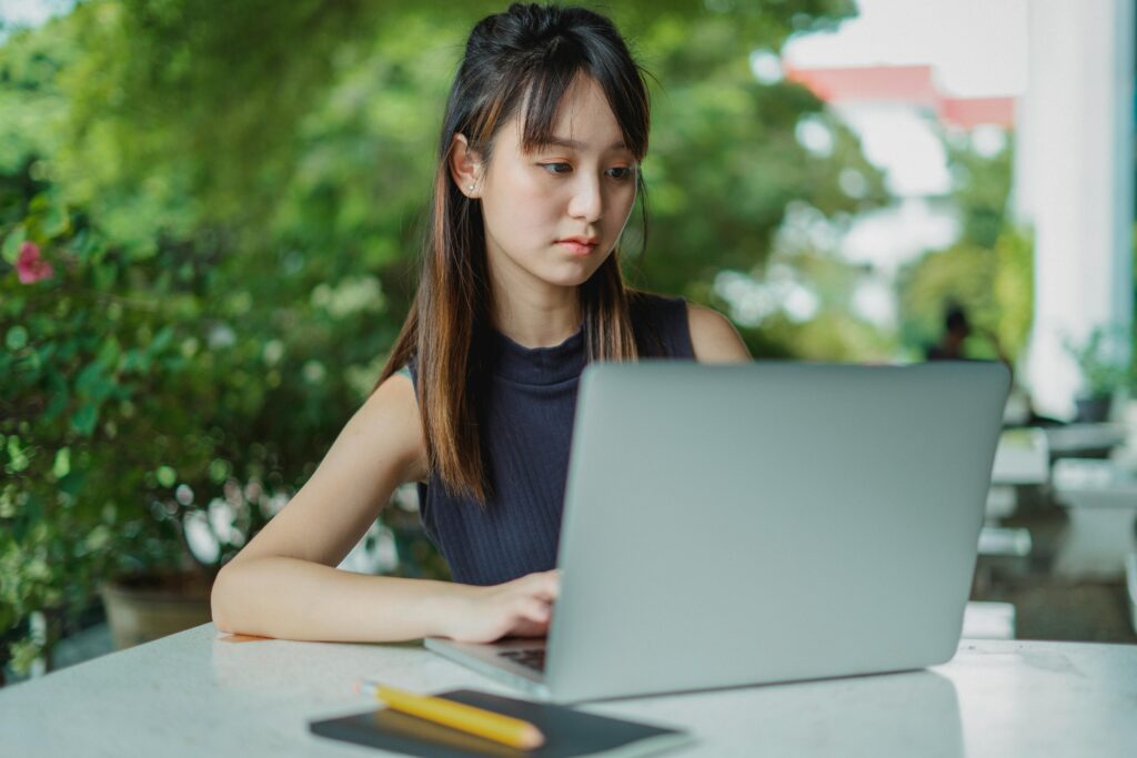 Young woman working on her laptop while her book and pen is on the table