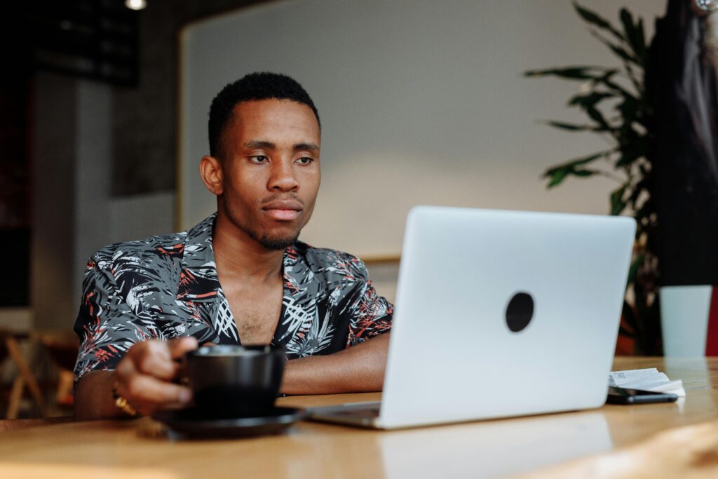 Man Working on a Laptop While Holding Cup of Coffee